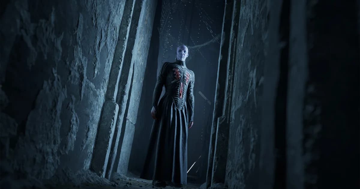 Pinhead in a long black robe standing in a narrow stone doorway lit cold blue
